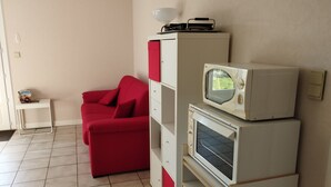 Un espacio habitable compacto con un sofá rojo, armarios blancos y un microondas encima.