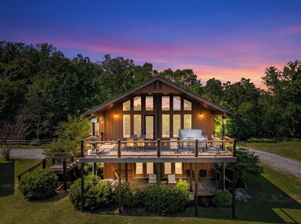 A two-story wooden cabin with a deck, large windows, and outdoor seating.