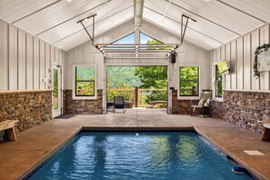 An indoor swimming pool with stone walls, a bench, and a view of greenery outside.