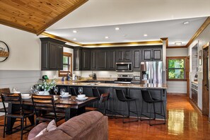 A modern kitchen with dark cabinetry, stainless steel appliances, and a wooden dining area.