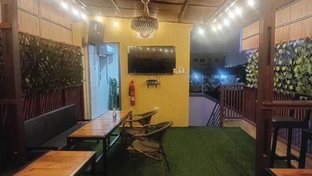 A restaurant with wooden tables and chairs, a flat-screen TV mounted on the wall, and a fire extinguisher on the wall. - Ostee Lodge (North Legon)
