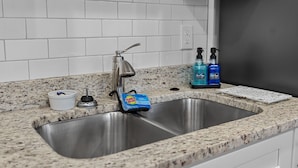 A kitchen with a stainless steel sink, granite countertop, white tiled backsplash, and a white cabinet above the sink.