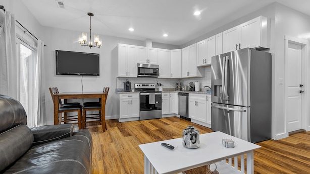 A modern kitchen with white cabinets, stainless steel appliances, and a dining area with a leather couch and wooden table.