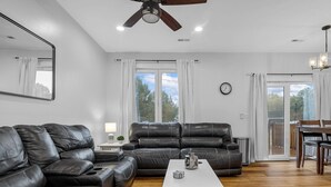 A spacious living room with a black leather sofa, a white coffee table, and a ceiling fan.