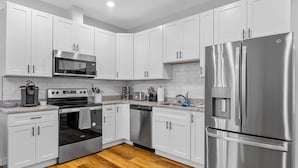 A modern kitchen with white cabinets, stainless steel appliances, and a wooden floor.