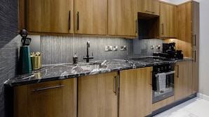 Cozinha moderna com armários de madeira, bancada de mármore preto, eletrodomésticos de aço inoxidável e forno embutido.