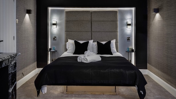 Quarto de hotel moderno com uma cama grande, duas mesas de cabeceira e uma mesinha de apoio de mármore.