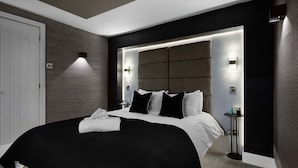 Quarto de hotel moderno com cama grande, mesa de cabeceira e luminária fixada na parede.
