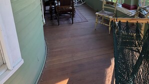 Eine überdachte Veranda mit Esstisch und Stühlen, einem Deckenventilator und großen Fenstern mit Blick auf den Garten.