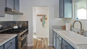 A modern kitchen with a gas stove, oven, and stainless steel cabinets. There is a sink with a faucet and a window above it. - Stylish Bungalow Steps to Sand & Downtown MB (Manhattan Beach)