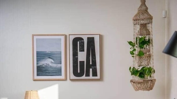 A cozy living room with a wooden coffee table, a leather armchair, a wicker hanging plant, and framed artwork on the wall. - Stylish Bungalow Steps to Sand & Downtown MB (Manhattan Beach)