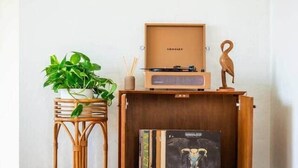 A corner of a room with a wooden sideboard, a wicker stool with a plant, and a framed picture on the sideboard. - Stylish Bungalow Steps to Sand & Downtown MB (Manhattan Beach)