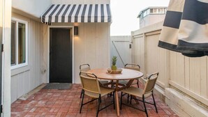A patio with a round wooden table, four wicker chairs, and a striped awning. - Stylish Bungalow Steps to Sand & Downtown MB (Manhattan Beach)