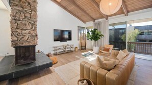 A living room with a stone fireplace, a television, a sofa, and a large window.