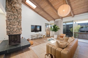 A living room with a stone fireplace, a television, a sofa, and a large window.