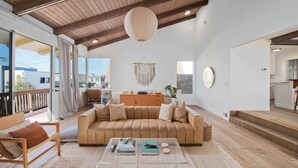 A spacious living room with a wooden ceiling, a large sofa, a coffee table, and a view of the outside.