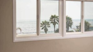 Ein Zimmer mit großem Fenster zum Meer, einem Stuhl und einem Bett mit Hut darauf.