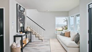 Ein modernes Wohnzimmer mit Treppe, einer Couch und einem großen Fenster mit Blick auf den Strand.
