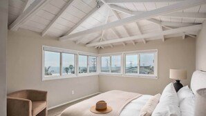 Ein Schlafzimmer mit einem großen Bett, einem Sessel, einer Lampe und Meerblick durch große Fenster.