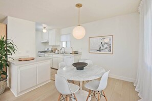 A modern kitchen with white cabinetry, a round marble dining table, and a pendant light. - Rooftop w/ Ocean Views, 2 Bedroom Beach Townhouse (Manhattan Beach)