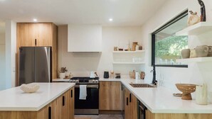 Une cuisine moderne avec des meubles en bois, un réfrigérateur en acier inoxydable, une cuisinière à gaz et une fenêtre donnant sur un espace verdoyant.