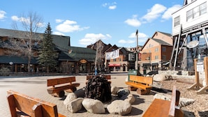 A wooden bench area with a fire pit, surrounded by rocks, in a town square with buildings in the background. - Ac39k4 (Keystone)