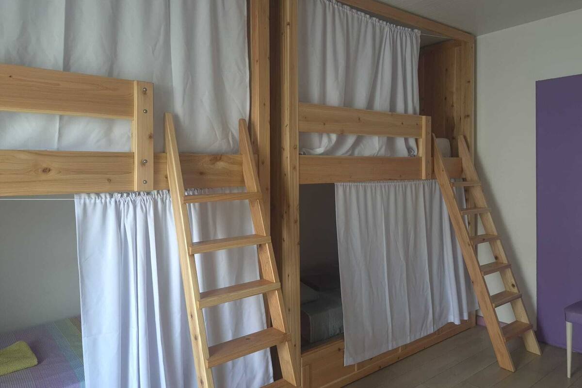 Een stapelbed met houten frames en witte gordijnen, een houten ladder en een paarse muur.