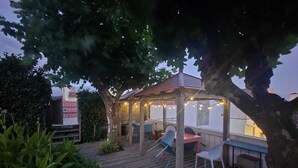A wooden deck with outdoor seating and string lights, surrounded by greenery. - Margarida & Miguel-Turismo e Alojamento (Ponta Delgada)