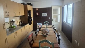 A compact kitchen with wooden cabinets, a built-in oven, and a dining area with a table and chairs. - Margarida & Miguel-Turismo e Alojamento (Ponta Delgada)