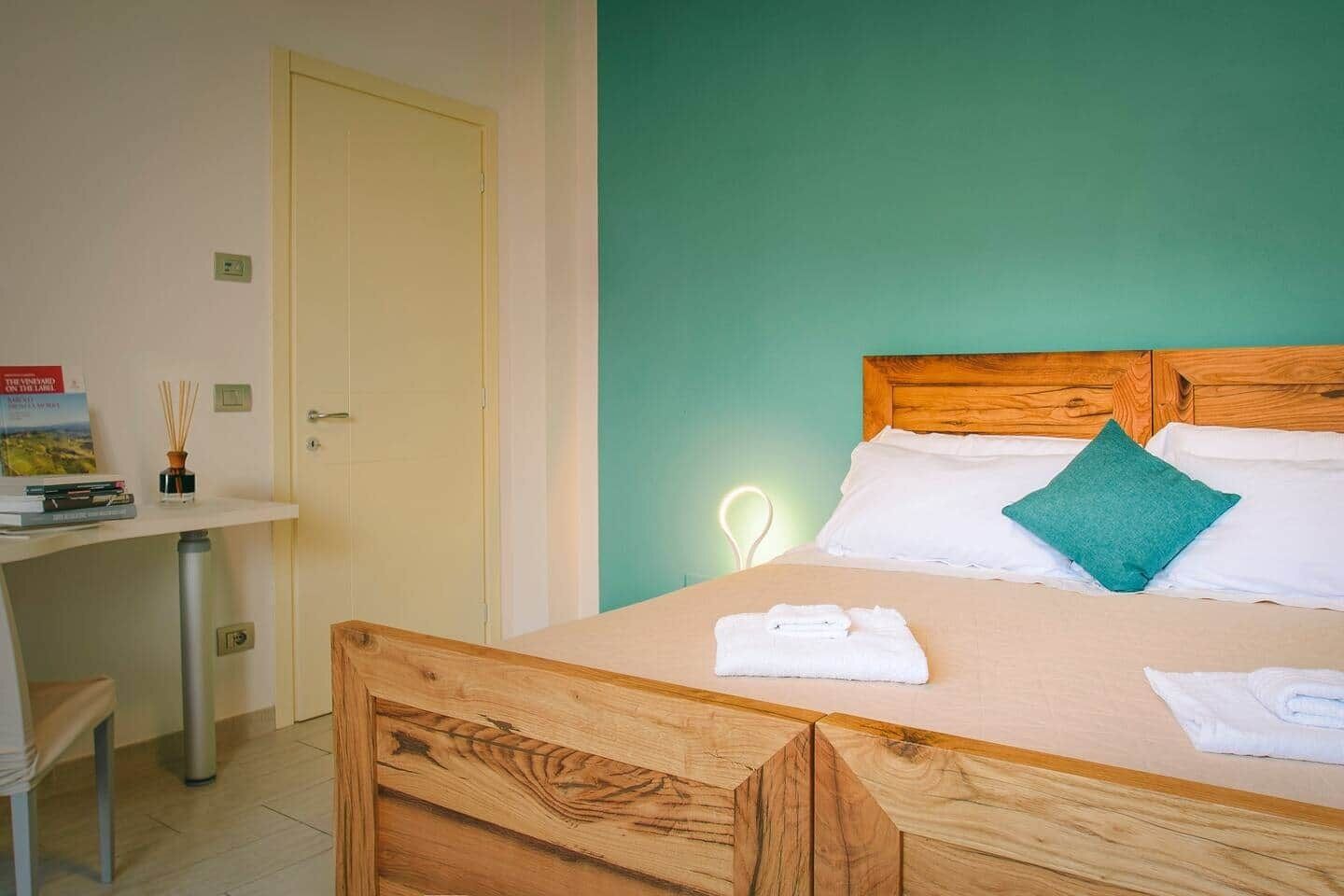 A bedroom with a wooden bed, a bedside table with books, a door, and a green wall.