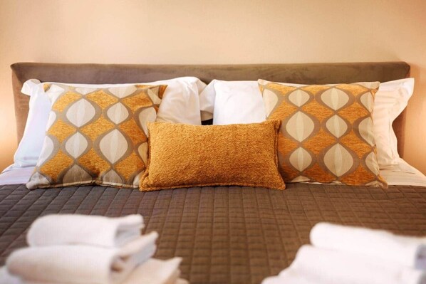 A neatly made bed with patterned pillows and a textured throw blanket.