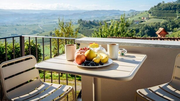 Un balcón con mesa lista para el desayuno, que incluye frutas y café, con vistas a un paisaje pintoresco.