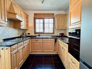 A kitchen with wooden cabinets, a black countertop, a window with blinds, and a stove. - Puebla Aida with Private Pool by Solrentspain (Mijas Costa)