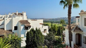Zona residencial con edificios blancos, una palmera y vistas a colinas distantes.