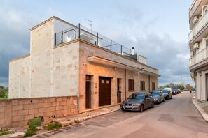 Vista del carrer amb un edifici que té un balcó, una porta de garatge i cotxes aparcats.