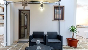 Un espacio de estar al aire libre cubierto con dos sofás de mimbre, una mesa con lámpara y una planta en maceta.