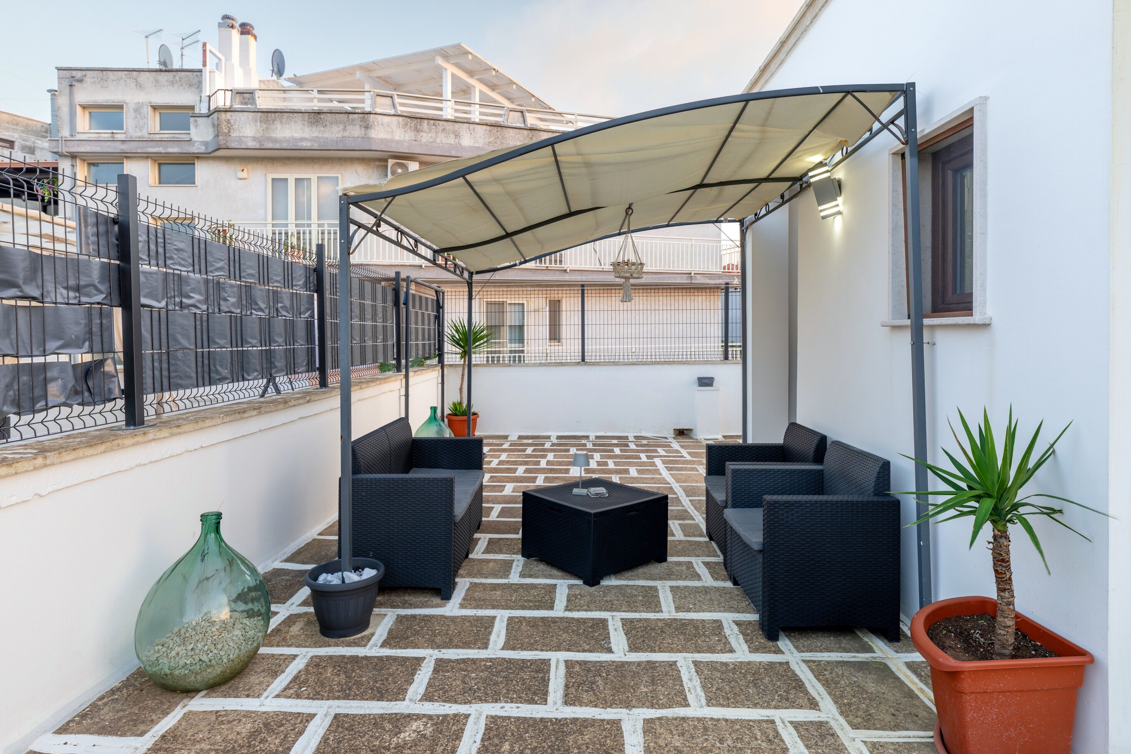 A rooftop patio with outdoor furniture, a covered area, and potted plants.