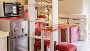 Une cuisine compacte équipée d’un réfrigérateur, d’un four à micro-ondes et d’une petite table à manger avec des chaises rouges.
