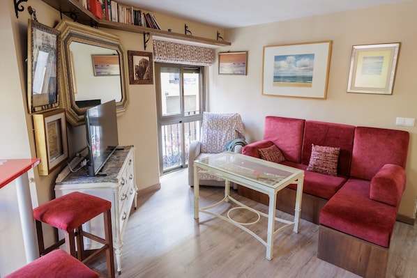 A living room with a red sofa, a glass coffee table, a white dresser, and a TV on a wooden cabinet.