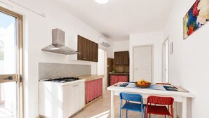 A modern kitchen with a gas stove, a built-in oven, and a stainless steel range hood. There is a dining table with two chairs and a fruit bowl on it. - Apartment 'Francesca, Bilo A' with Shared Terrace, Wi-Fi and Air Conditioning (Peschici)