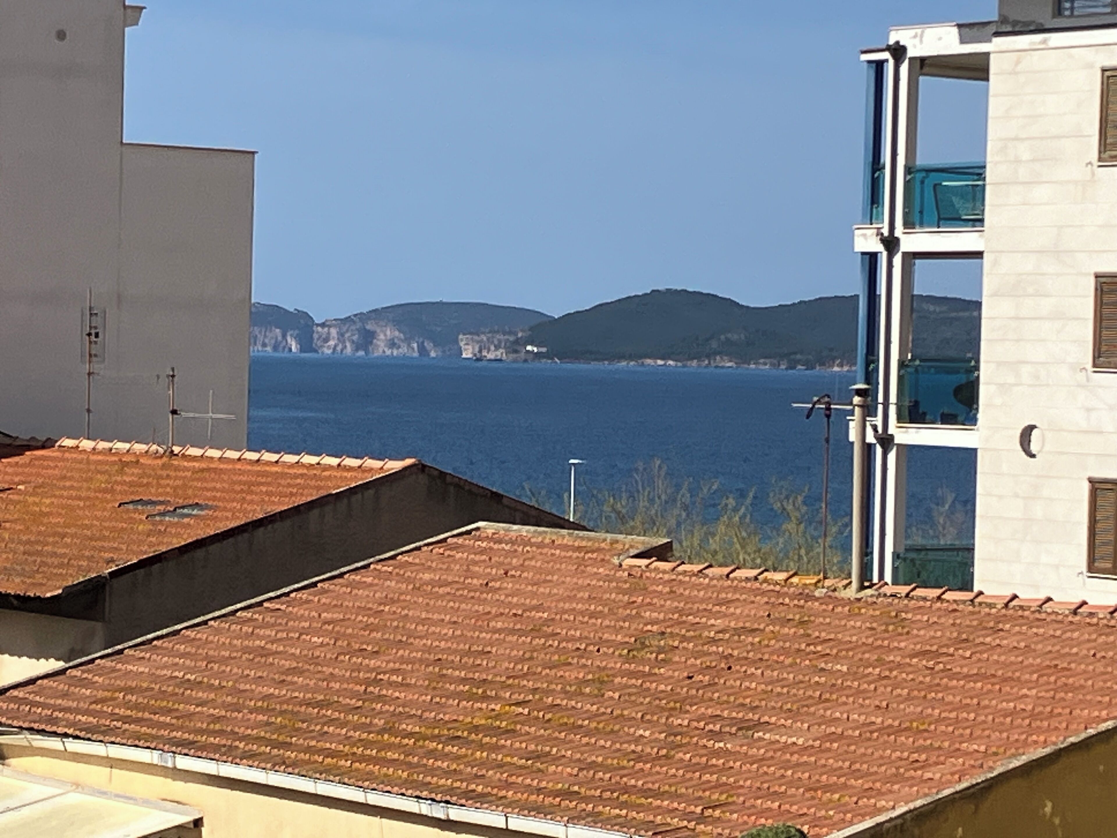 A coastal building with a tiled roof and a view of the sea and distant hills.