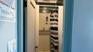 A narrow hallway with a blue door frame, a shower area with a striped curtain, and a wall-mounted emergency exit sign. - City Limits Inn Hotel (Yorkton)