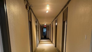 A long, narrow hallway with doors on both sides, a light fixture on the ceiling, and a visible exit sign. - City Limits Inn Hotel (Yorkton)