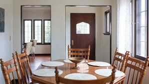 Une salle à manger avec une table et des chaises en bois, un lustre et une vue sur l’extérieur grâce à de grandes fenêtres.