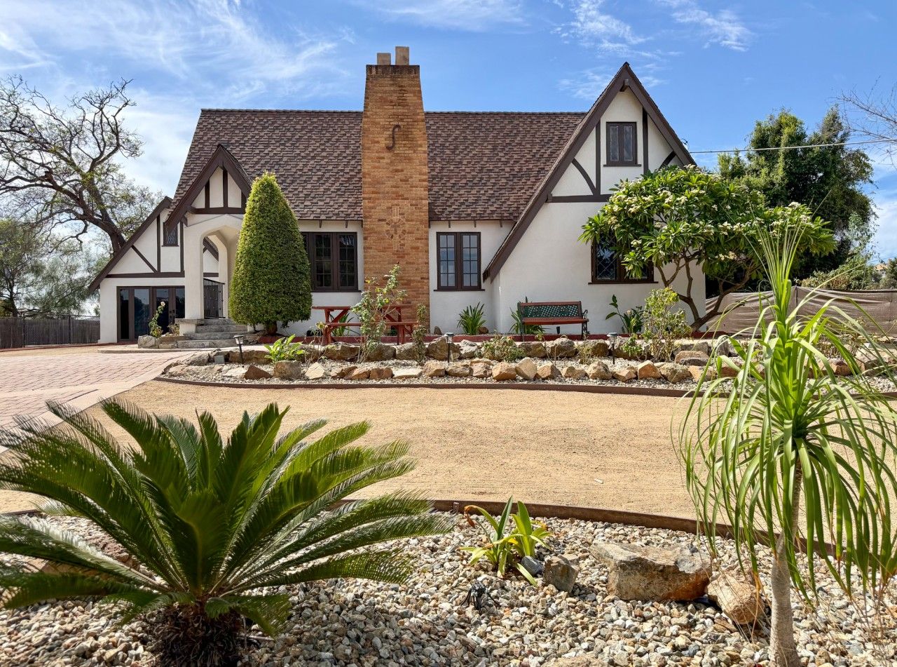 A house with a prominent chimney, a well-maintained garden with various plants, and a paved driveway.