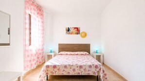Una camera da letto con un letto, abat-jour, un quadro appeso al muro e una finestra con tenda a cuori rosa.