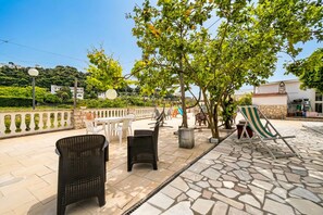 Zona patio esterna con sedie in vimini, un tavolo e una poltrona da relax a righe.