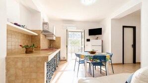 Una cucina moderna con zona pranzo, una TV montata sopra il bancone e una porta che dà su un'altra stanza.