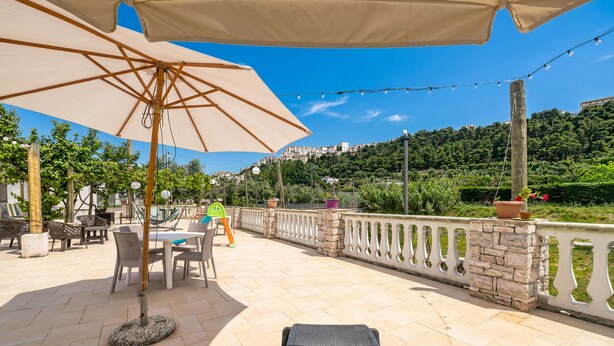 Una veranda esterna con poltrone relax, un tavolo e ombrelloni.