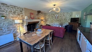 A rustic kitchen with a stone wall, wooden furniture, a fireplace, and a modern pendant light. - Gîte "La Prèze" - Deluxe 2 Bedrooms (n°4) (Rouzède)